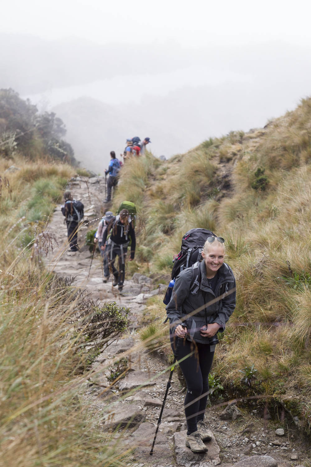 Manouk wandelt op een pad van de Inca Trail met haar backpack tussen het hoge gras