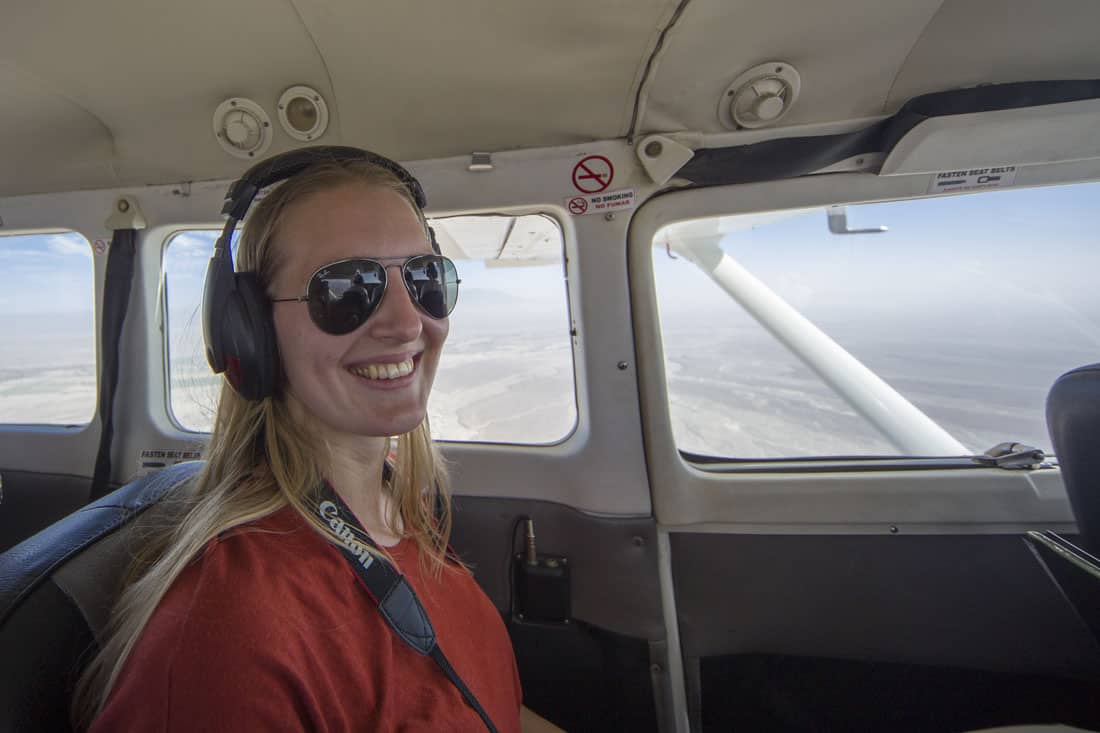 Manouk zit in een rood shirt met zonnebril op in een klein vliegtuigje dat over de Nazcalijnen vliegt, met een koptelefoon op om de piloot te horen.