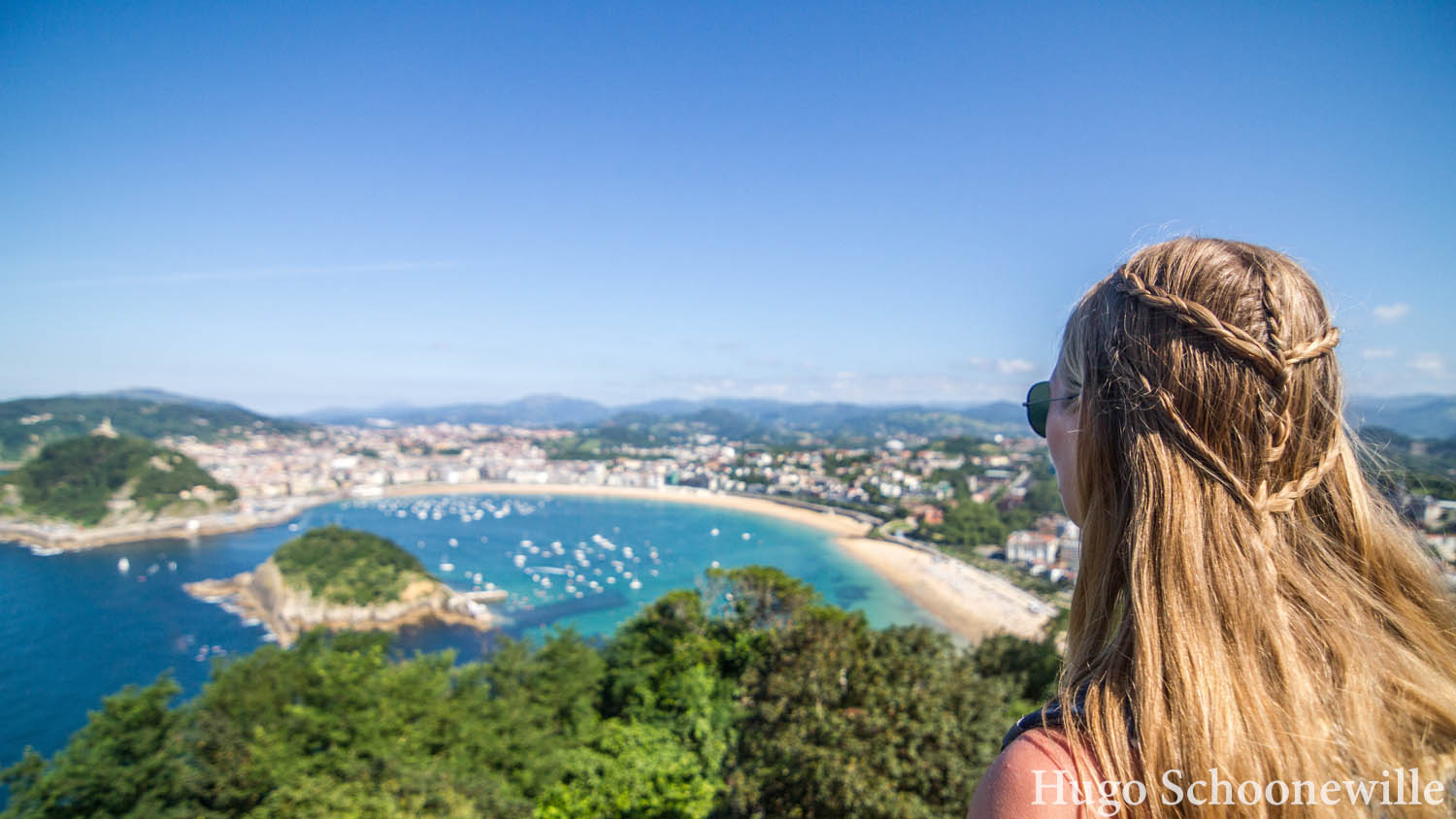 Uitkijkend over de baai van San Sebastián met helderblauw water en zon: meisje met blonde vlechten.