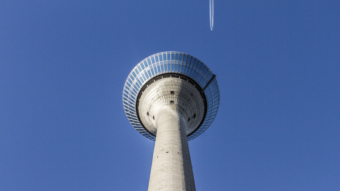 De Rheinturm in Düsseldorf van onderaf gezien, met een passerend vliegtuig.