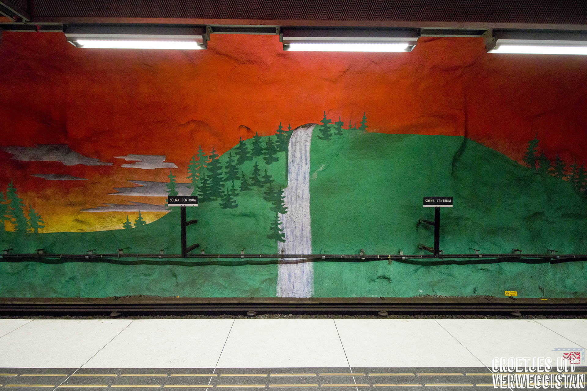 Metrokunst in Stockholm in metrostation Solna Centrum: oranjerode lucht en een landschap in het groen op de muren van het metroplatform.