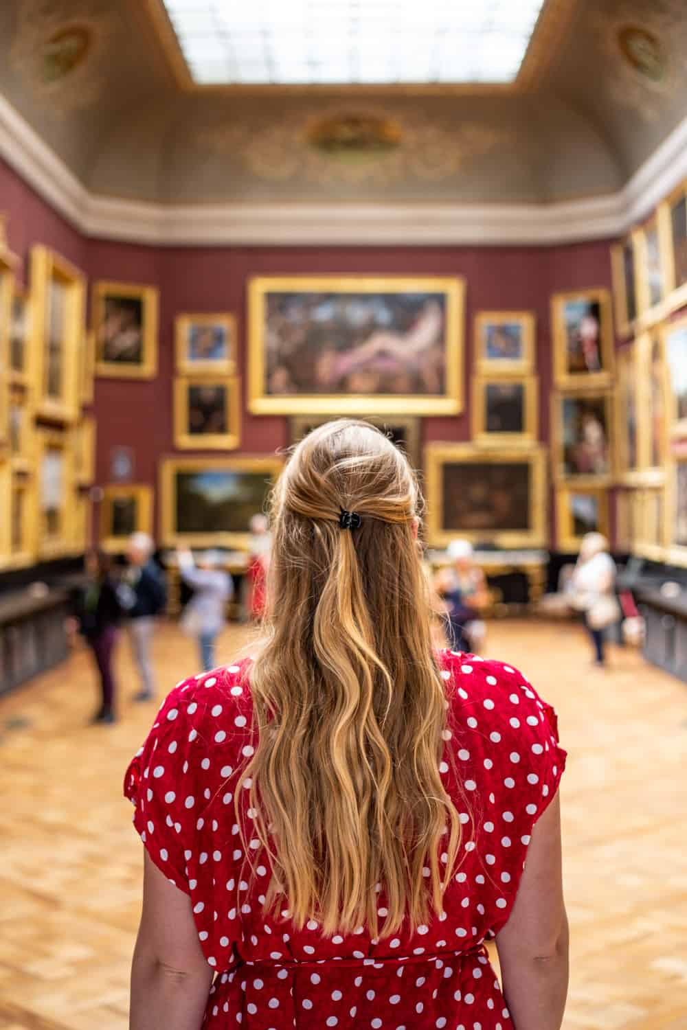 Manouk staat met haar rug naar de camera en kijkt uit over een zaal vol schilderijen in Musee Conde in Chateau de Chantilly