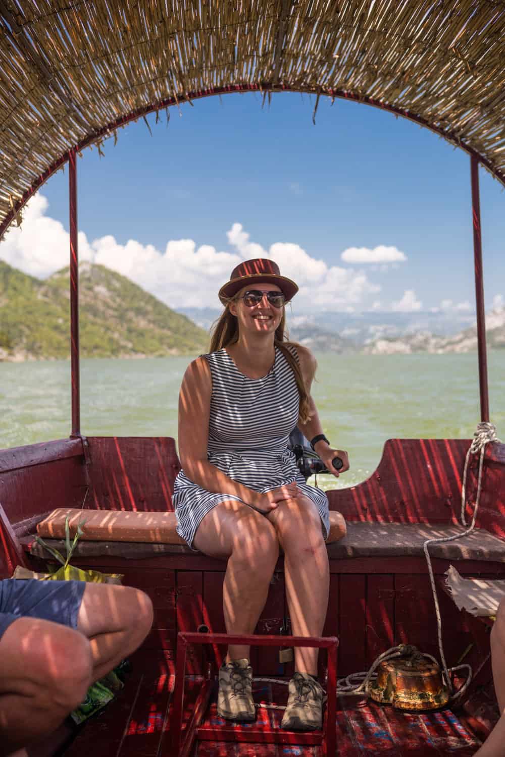 Manouk aan het roer van een houten boot met rieten dak op het Skadarmeer in Montenegro.