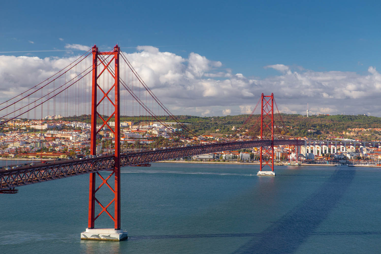 Rode brug in Lissabon over de rivier met Lissabon op de achtergrond.