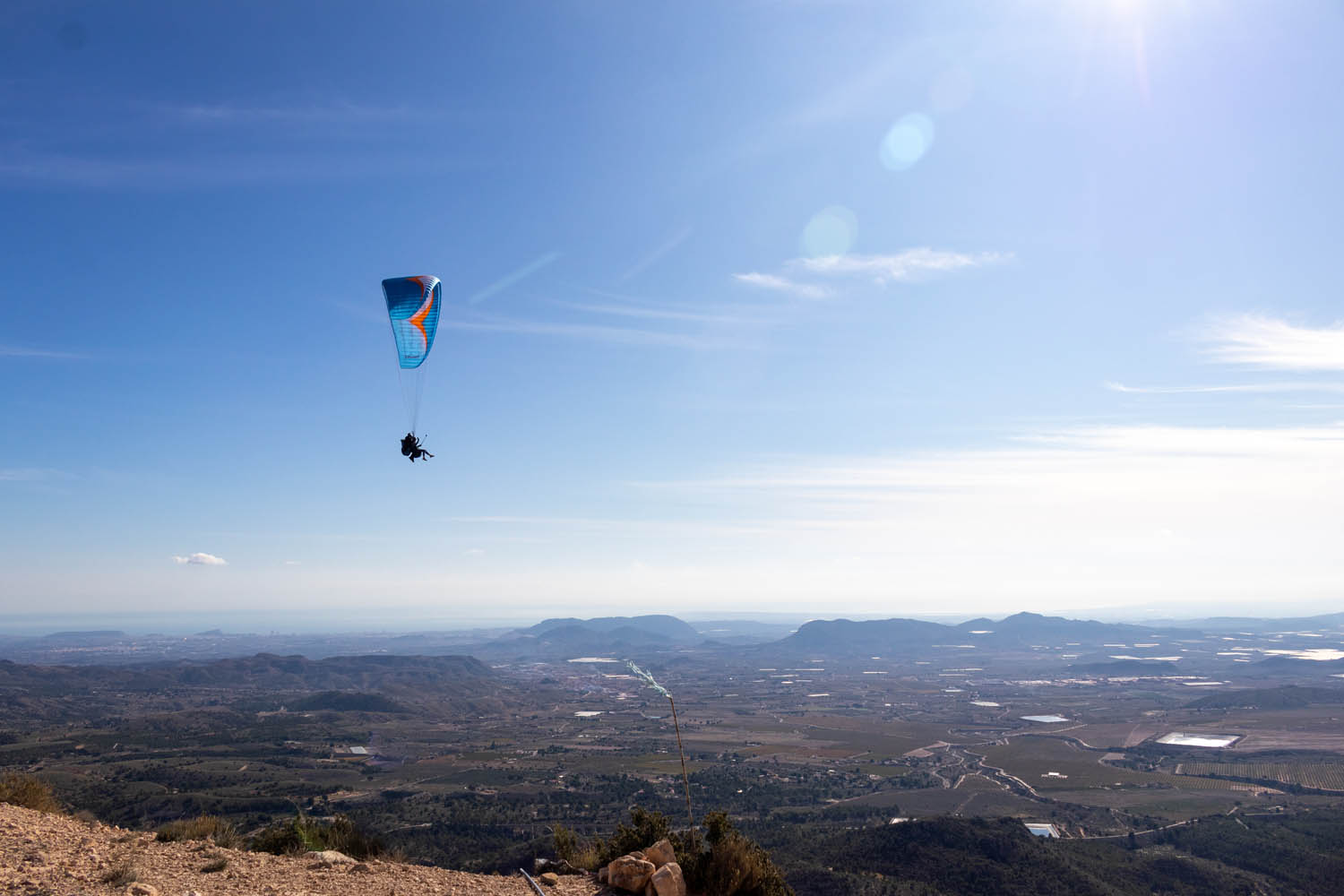 Blauwe paraglider hoog boven de horizon met Alicante op de achtergrond.