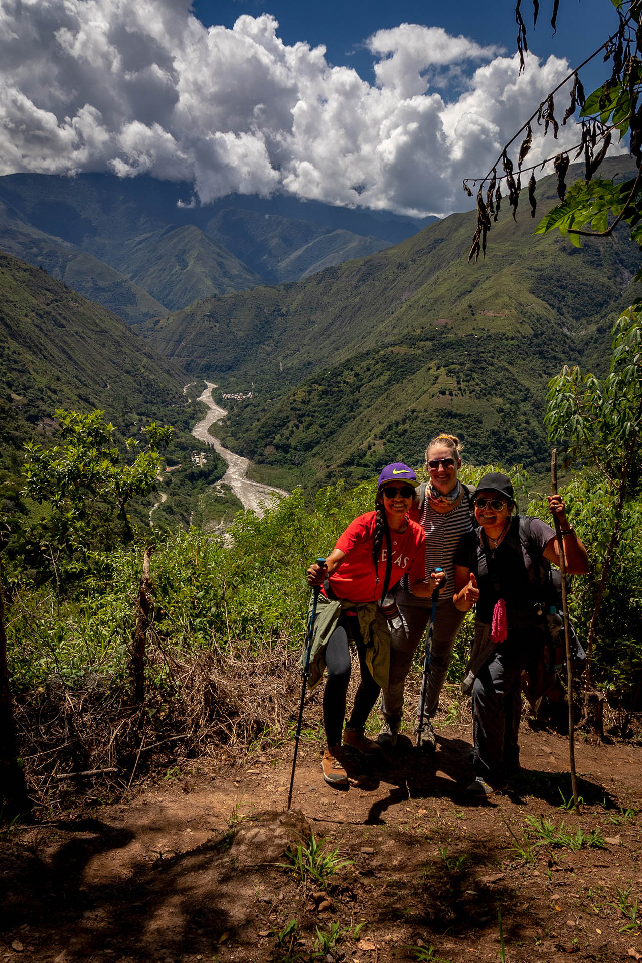 Drie vrouwen op een wandelpad langs de Inka Trail in Peru met uitzicht op een vallei met een rivier.