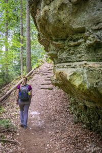 Manouk wandelt langs een rots in het bos op de Mullerthal Trail