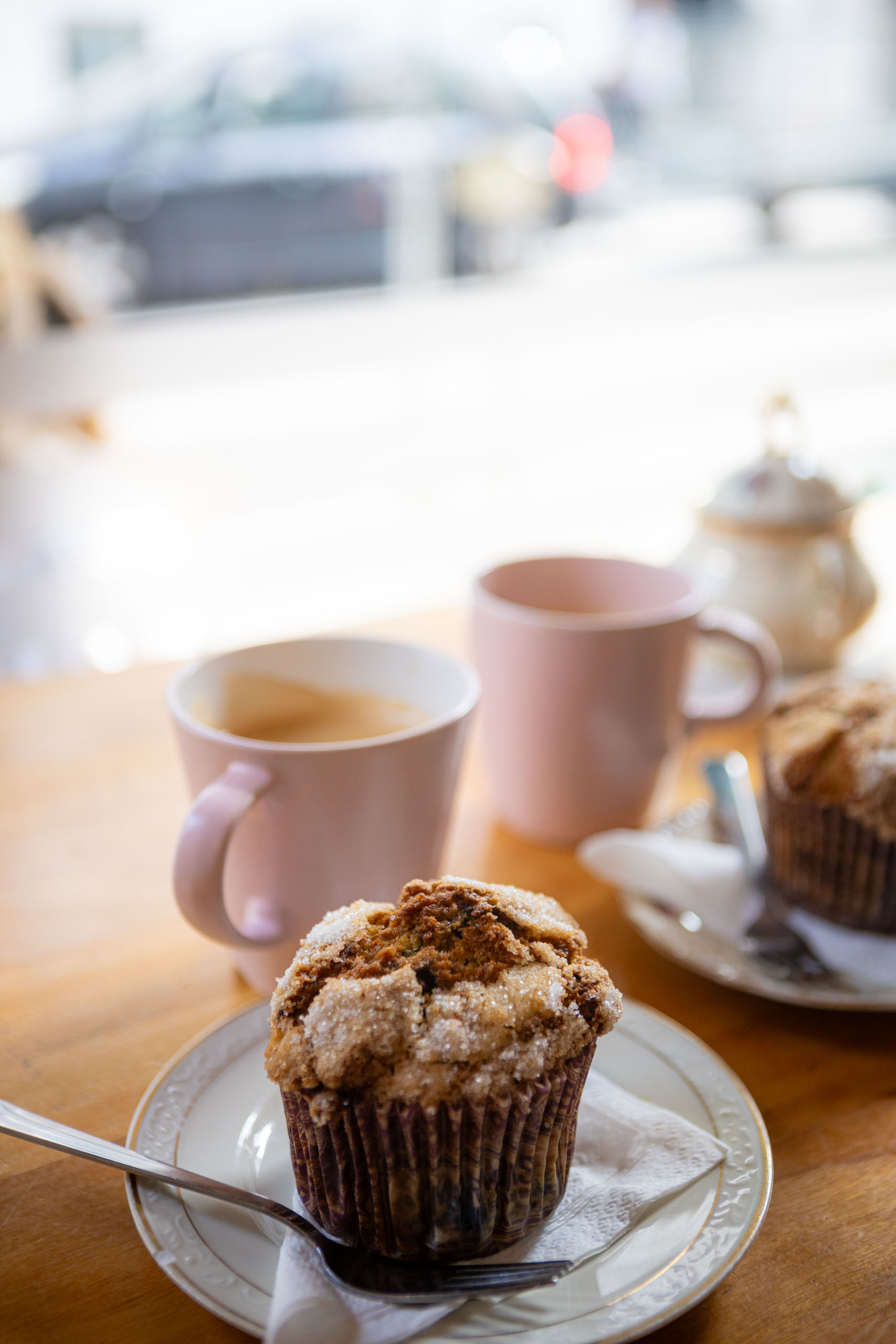 Roze kopjes koffie met muffins op een bar voor het raam