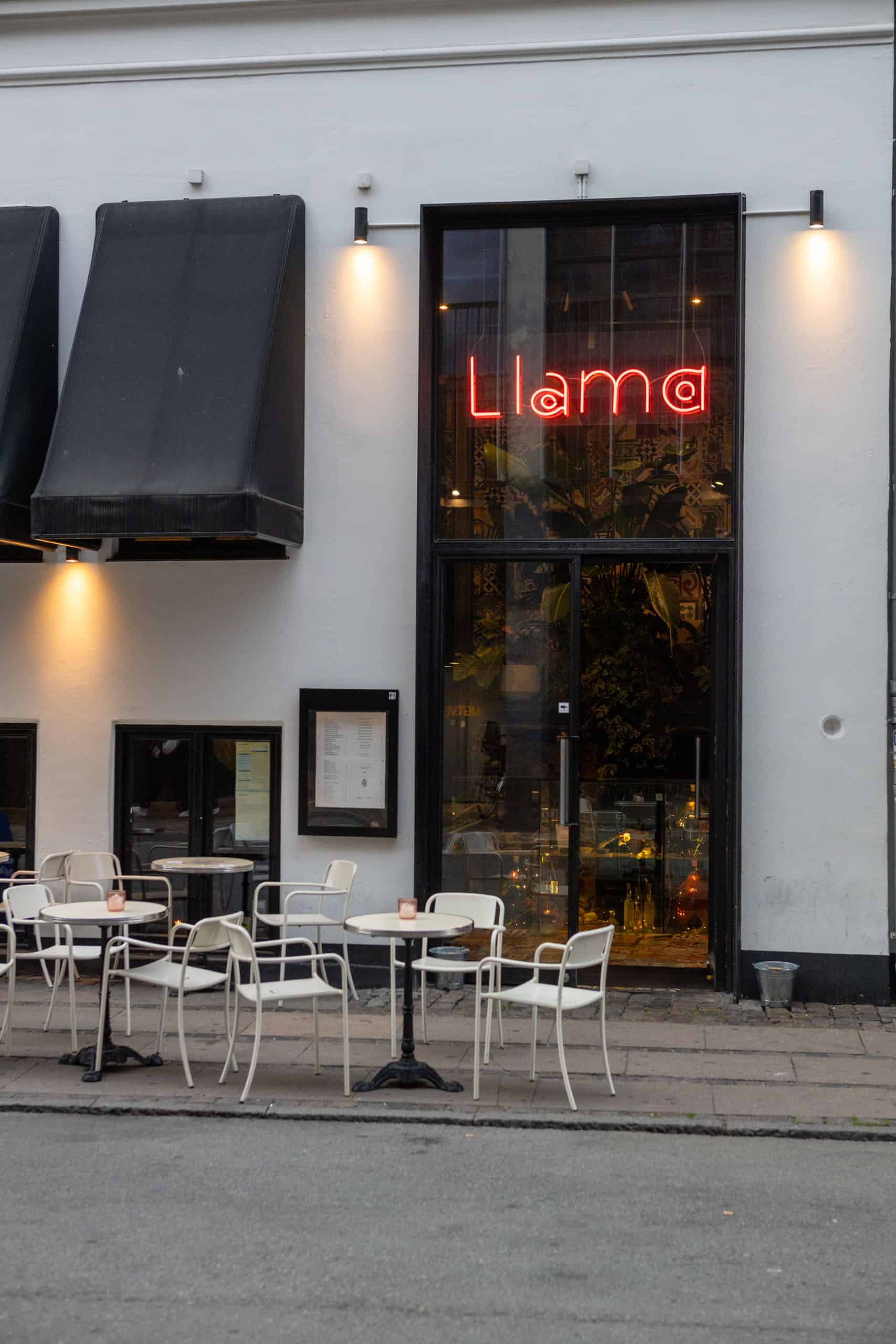 Voorzijde van restaurant Llama in Kopenhagen met witte muur, glazen deur en rode neonletters die Llama spellen