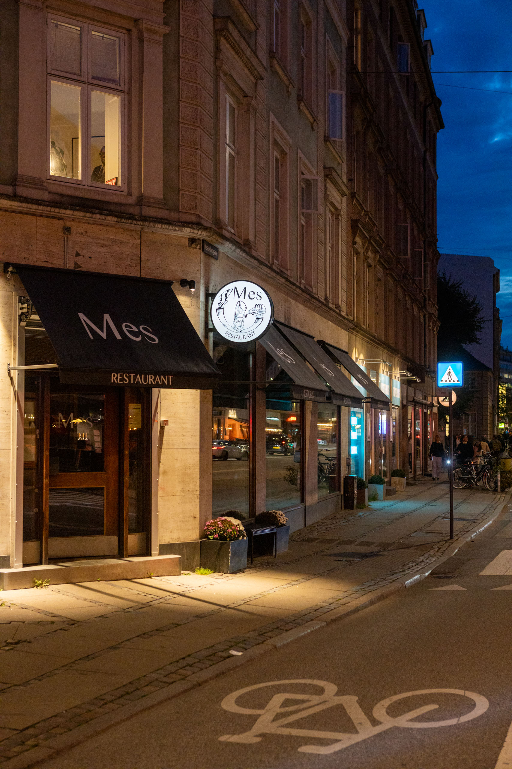 Voorzijde van restaurant Mes in Kopenhagen in de avonduren met de naam op een zwarte luifel