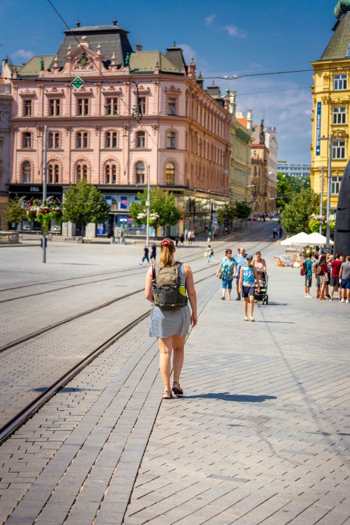Manouk loopt over plein Namesti svobody in Brno met roze en gele gebouwen op de achtergrond
