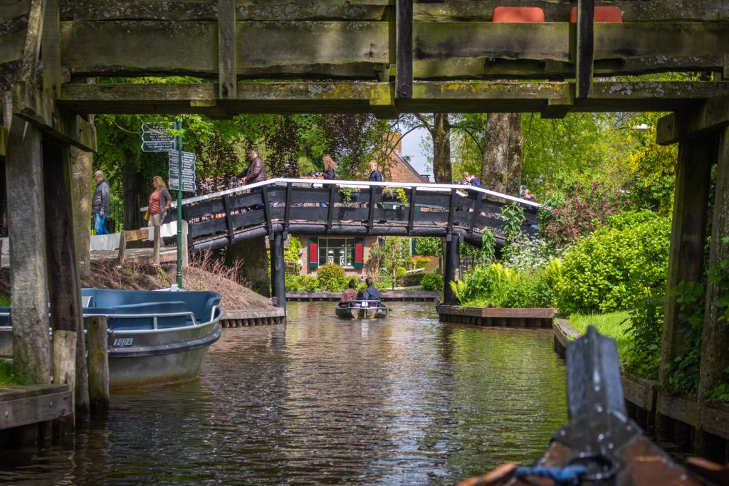 Doorkijkje onder een brug door over het water van Giethoorn met een bootje