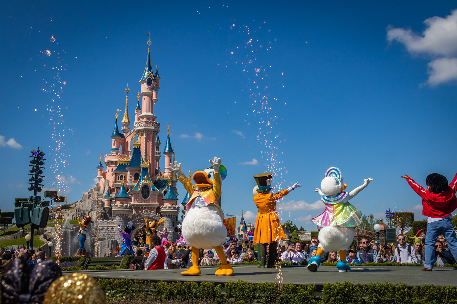 Podium op Central Plaza in Disneyland Parijs met het kasteel op de achtergrond en op het podium Donald, Katrien, Mad Hatter en dansers