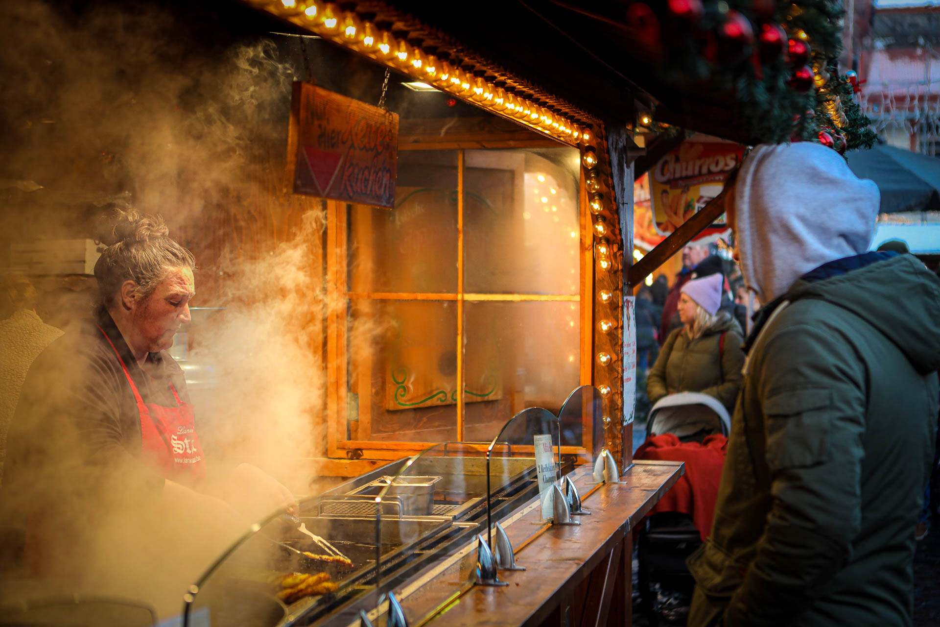 Vrouw staat gehuld in rook in een kraam en bakt reibekuchen op de kerstmarkt in Koblenz