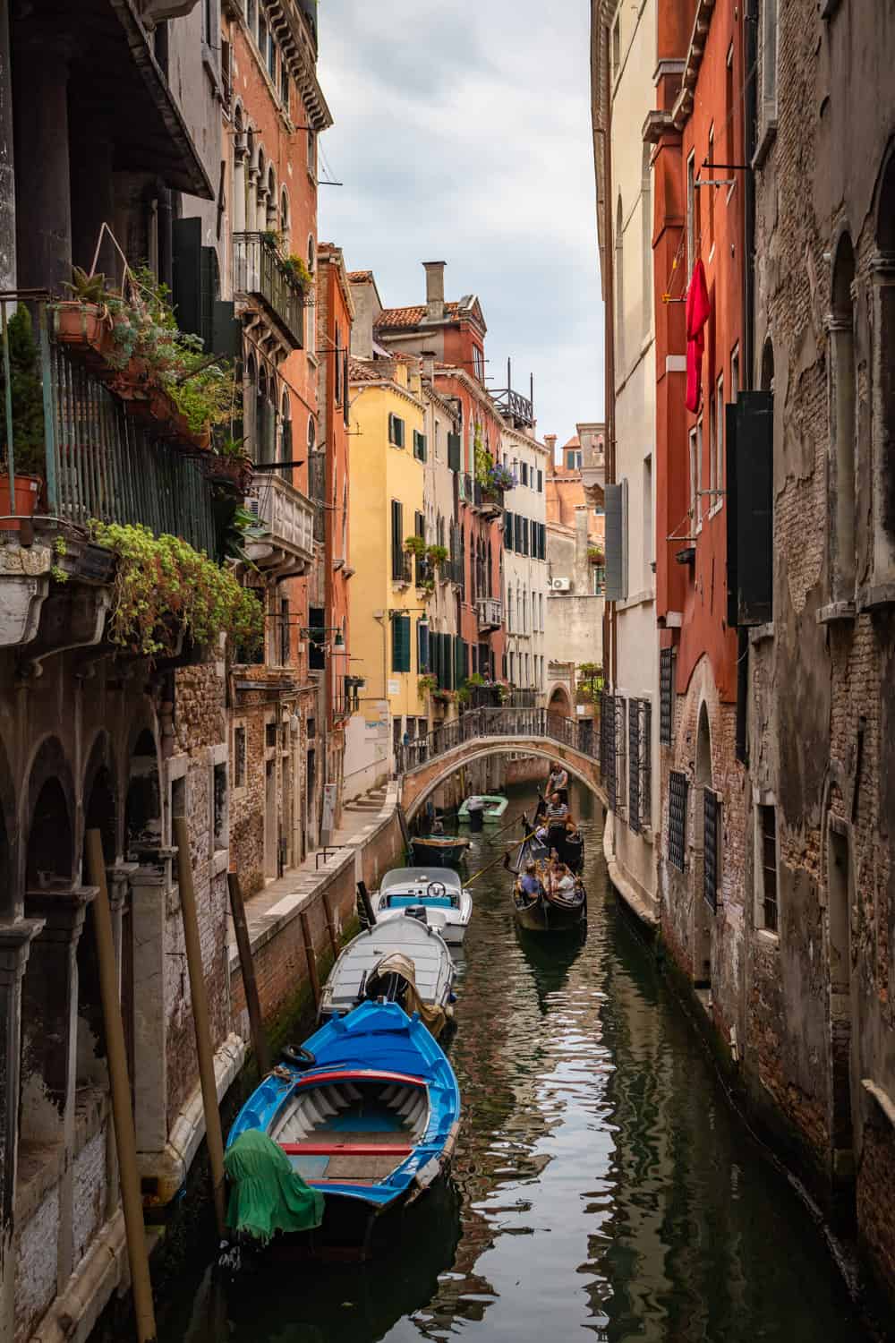 Smal steegje met water en boten langs de linkerkant met gekleurde huizen met planten voor de ramen in Venetië