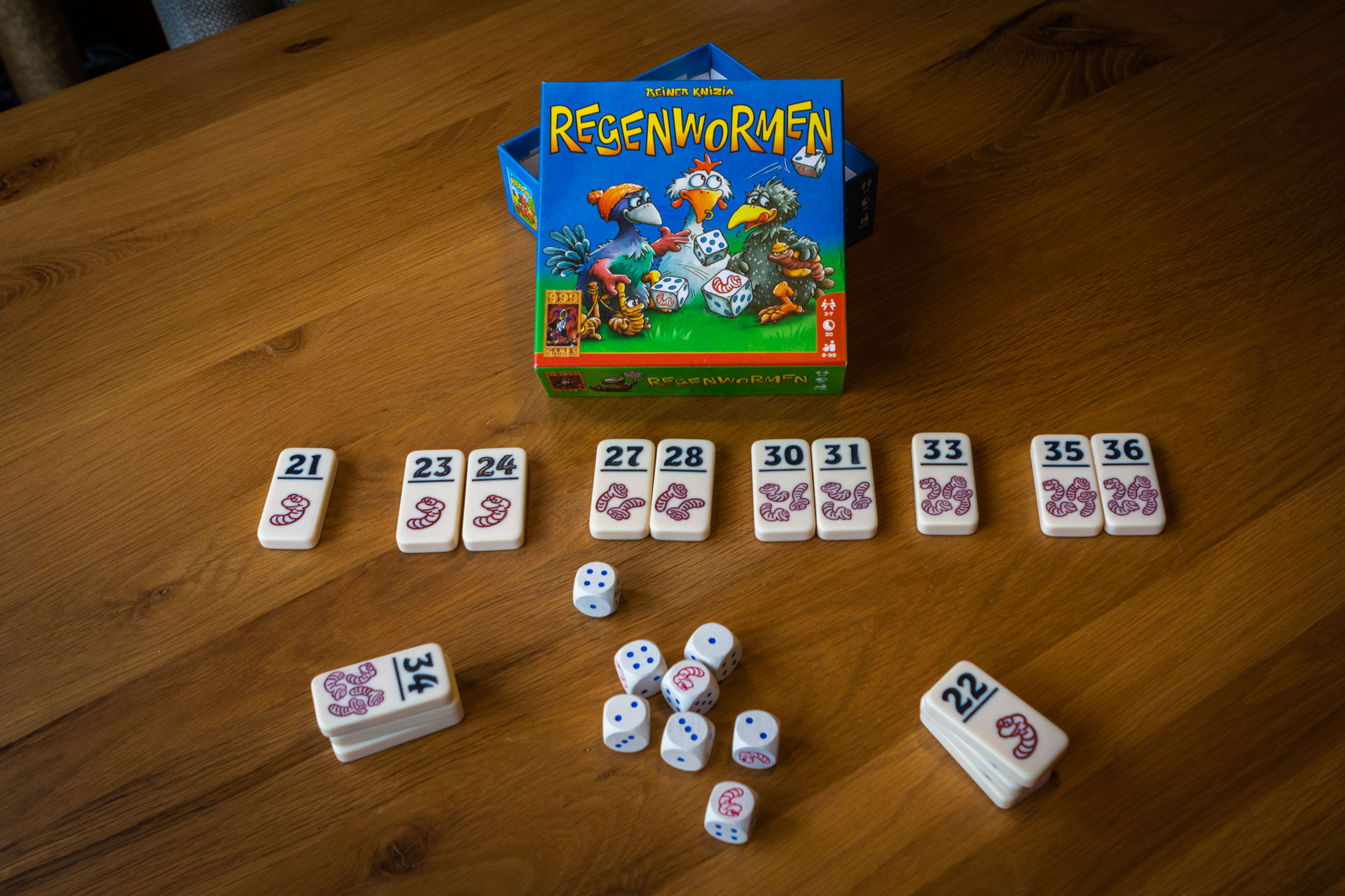 Het spel Regenwormen met doosje en tegeltjes en dobbelstenen op een tafel