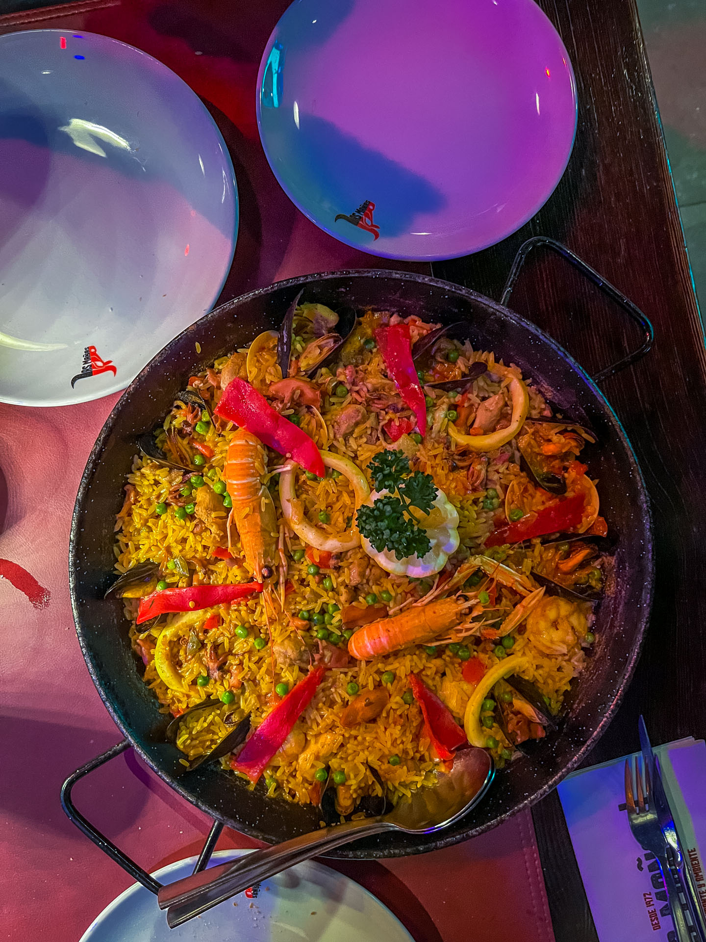 Paella in grote pan in het midden van de tafel in gekleurd licht bij restaurant Las Manas in Antwerpen