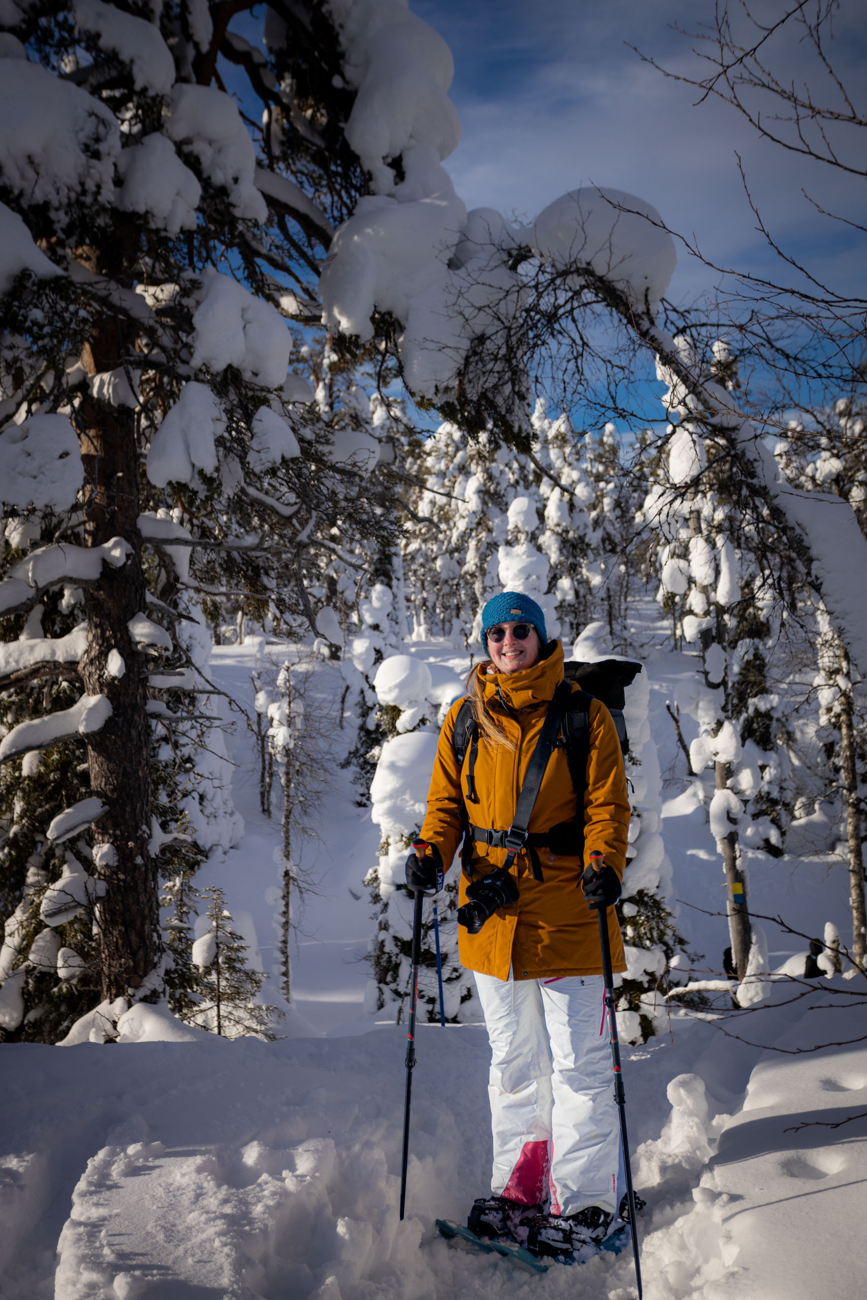 Wat te doen in Rovaniemi: Manouk wandelt in een gele jas tussen besneeuwde bomen richting de amethistmijn Lampivaara