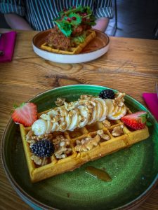 Wafel met banaan, aardbei en bramen op een groen bord met op de achtergrond een wafel met vegan kip bij Aloha in Leiden.