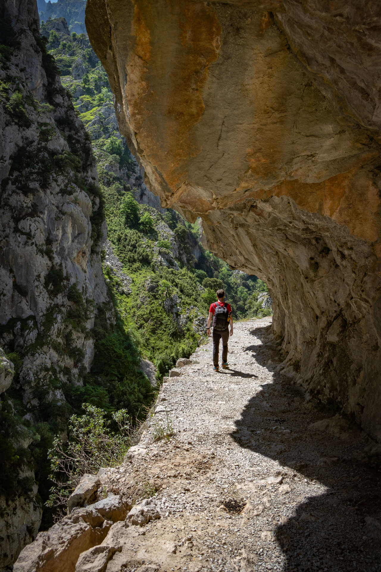 Hugo loopt onder een overhangende klif door op de Ruta del Cares in Spanje