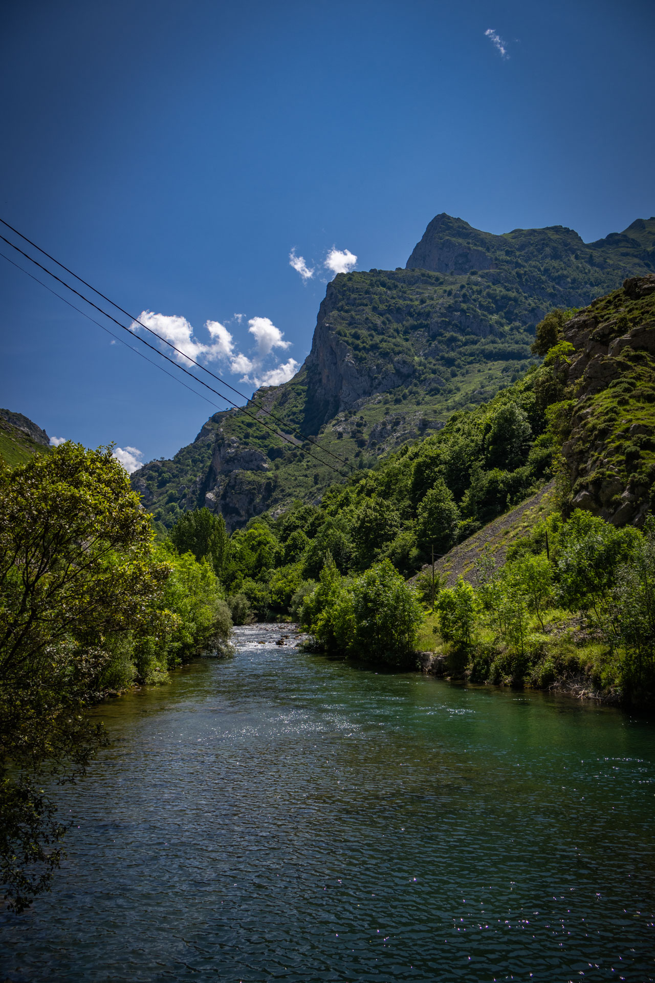 De rivier Cares stroomt rustig richting Caín, omring door groen.