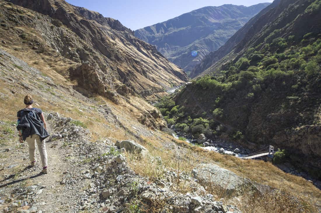 Manouk loopt een pad af in de Colca Canyon, met in de diepte de rivier Colca met een brug erover
