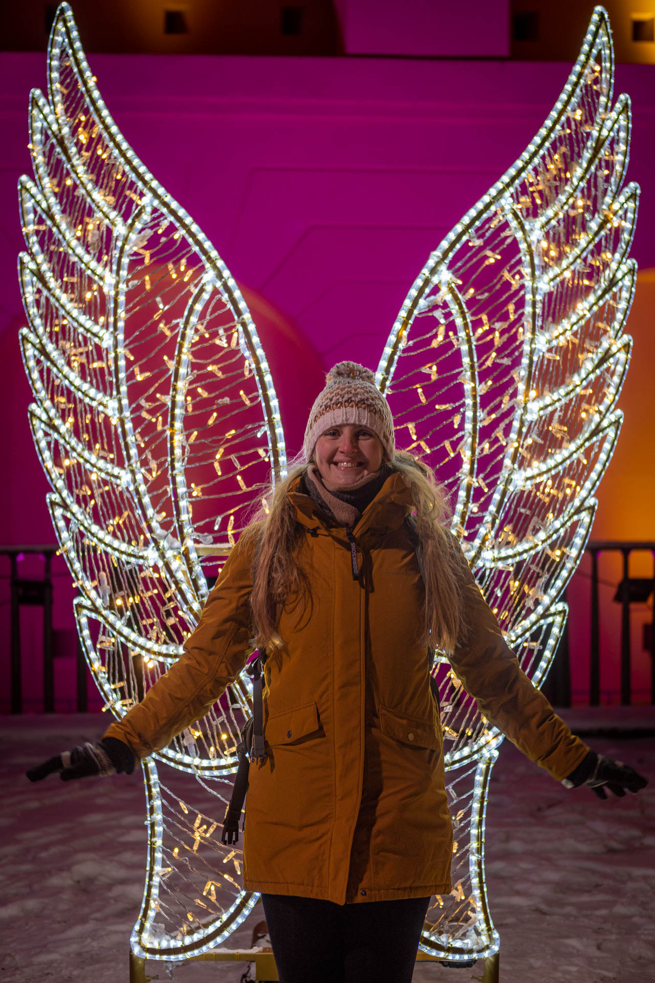 Manouk staat voor een lichtsculptuur van grote engelenvleugels met een roze verlichte muur erachter tijdens Christmas Garden Koblenz
