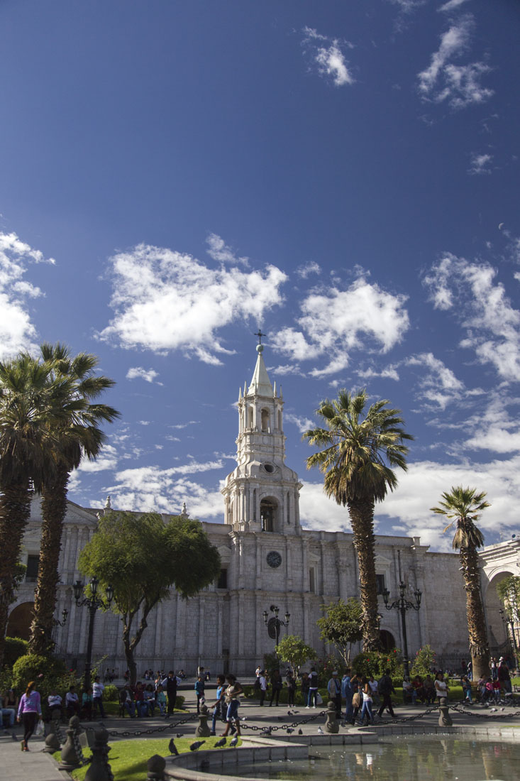Witte kathedraal aan een plein in Arequipa tegen een blauwe lucht met wolken
