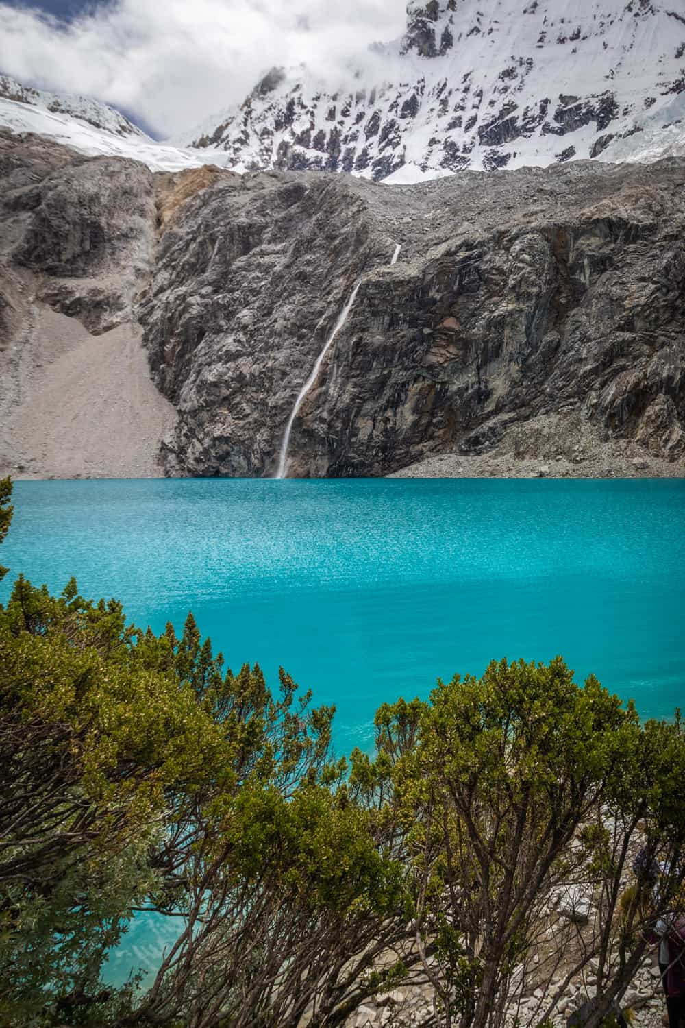 Blauw meer met besneeuwde bergen erachter en groene bosjes ervoor: Laguna 69 in Peru