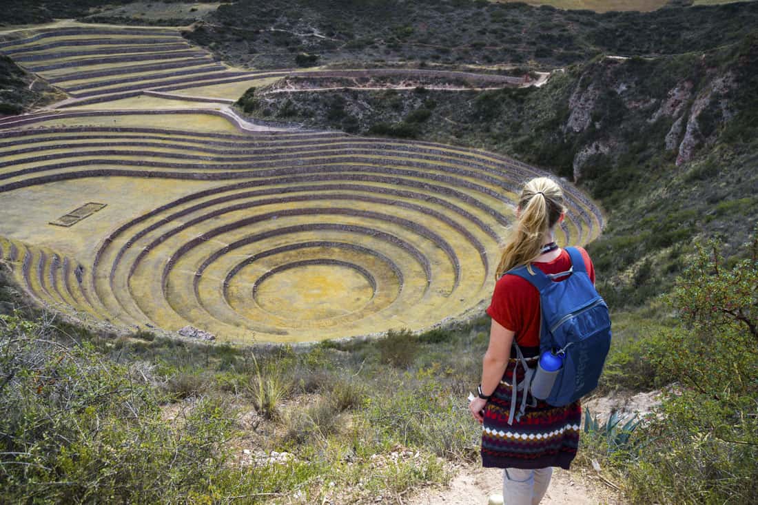 Manouk met een typisch Peruaanse trui om haar middel staat met de rug naar de camera en kijkt uit over cirkelvormige terrassen aangelegd door de Inca's in Moray