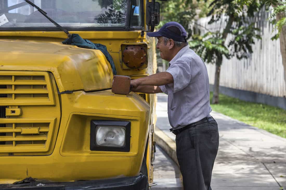 Buschauffeur staat naast de motorkap van een gele Amerikaanse schoolbus om de bus te poetsen