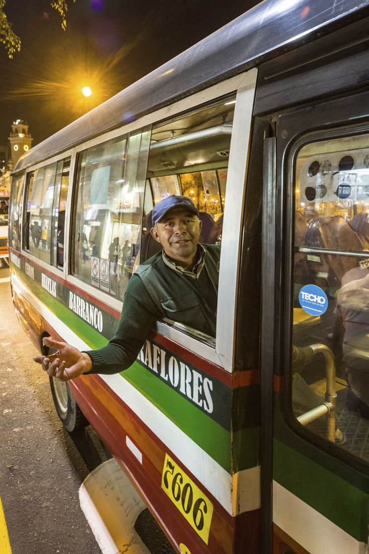 Buspersoneel hangt uit busraam in Lima en kijkt in de camera