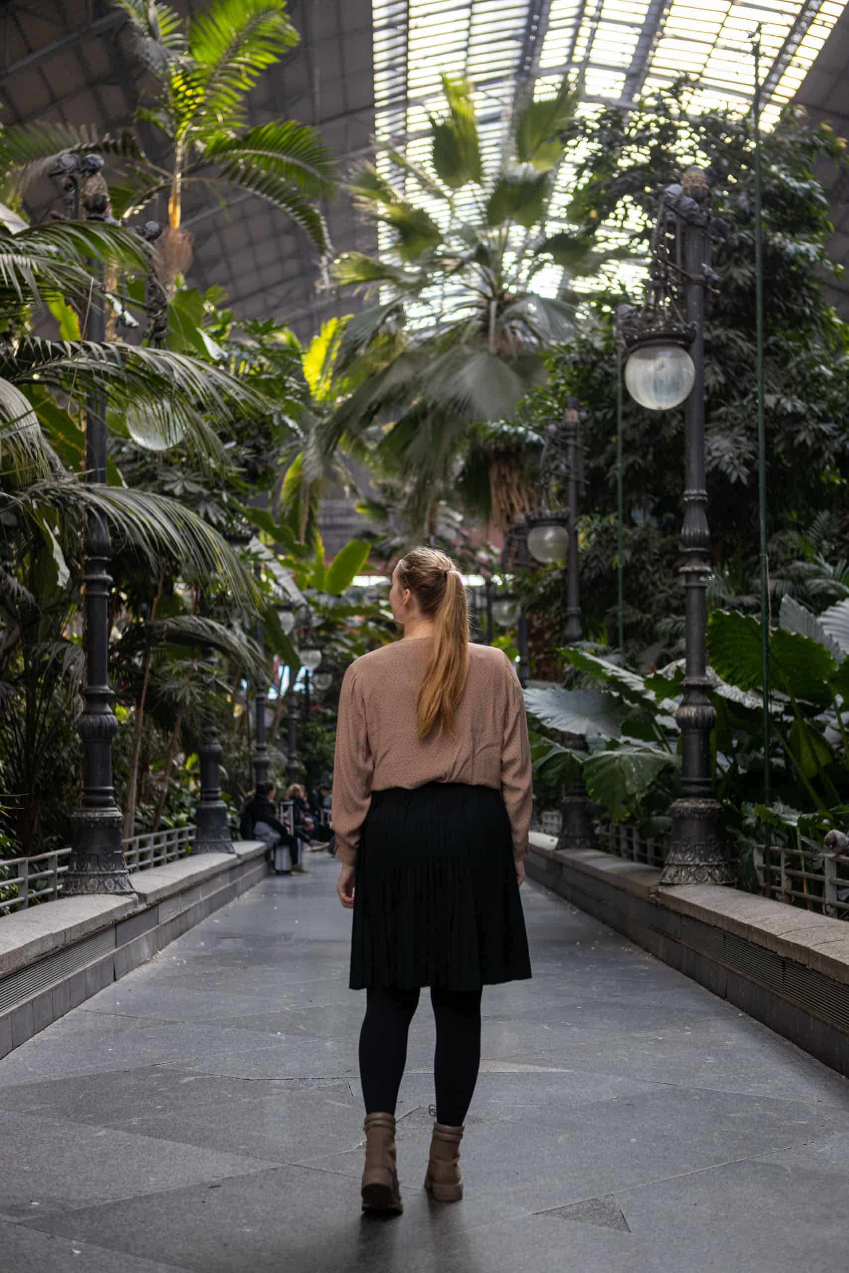 Manouk loopt met bruine blouse en zwarte rok over een pad door de botanische tuin in Atocha, met groen aan beide zijden.