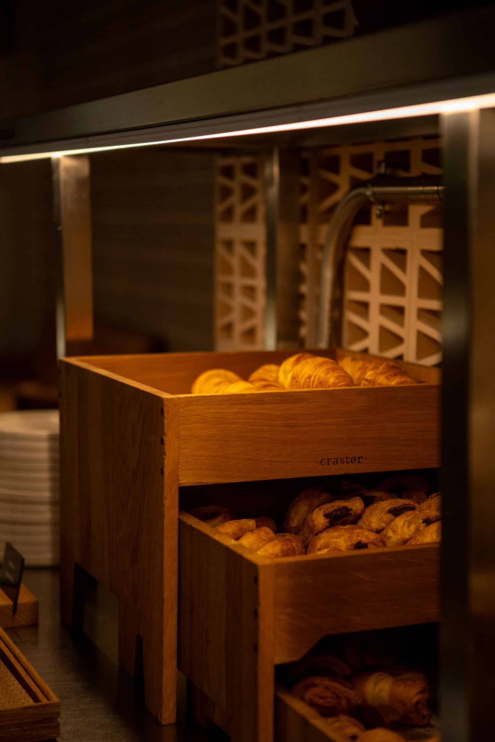 Houten bakken met verschillende soorten broodjes bij het ontbijtbuffet in The Social Hub Madrid
