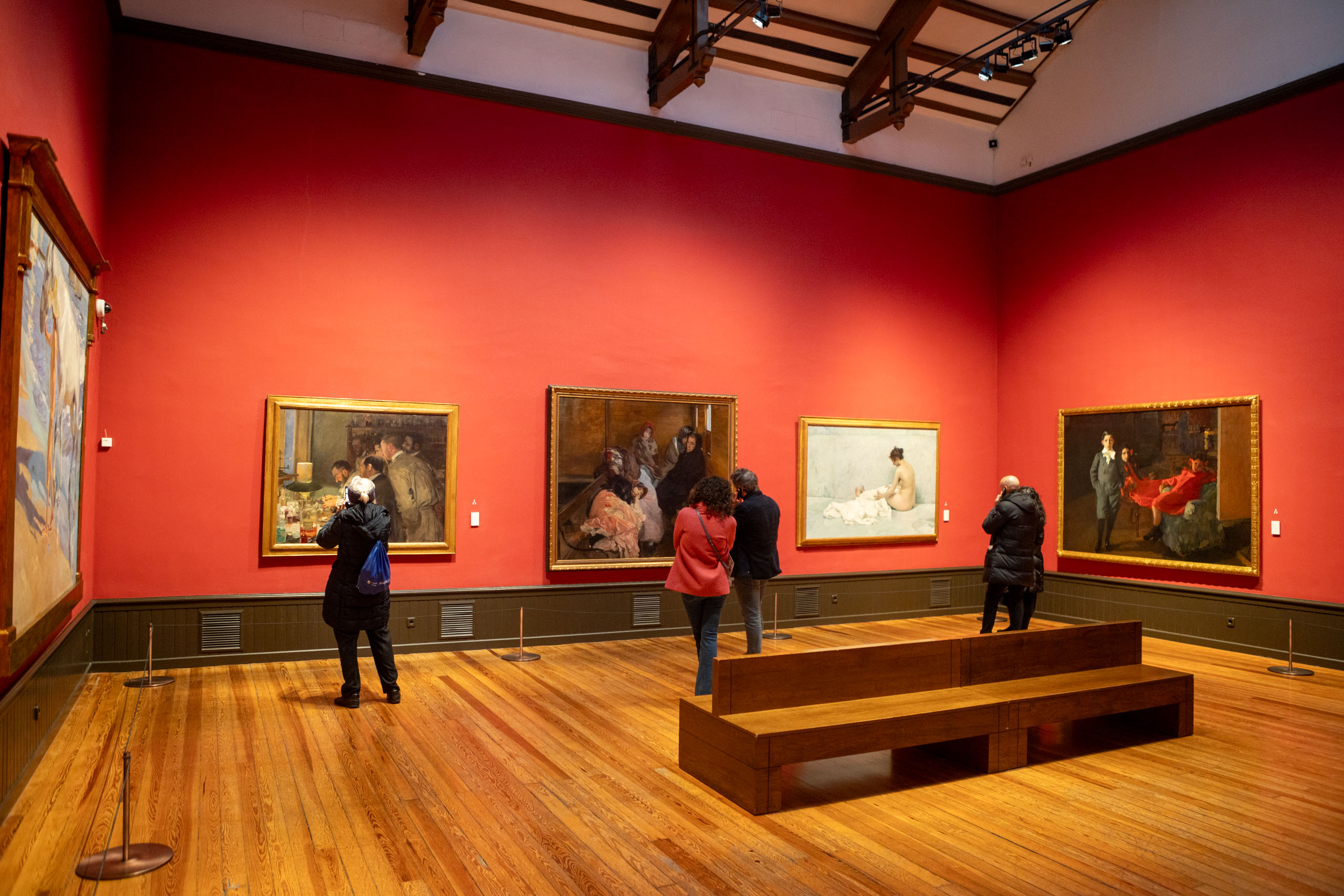 Eerste zaal in Museo Sorolla met rood/oranje muren met verschillende schilderijen en houten vloer