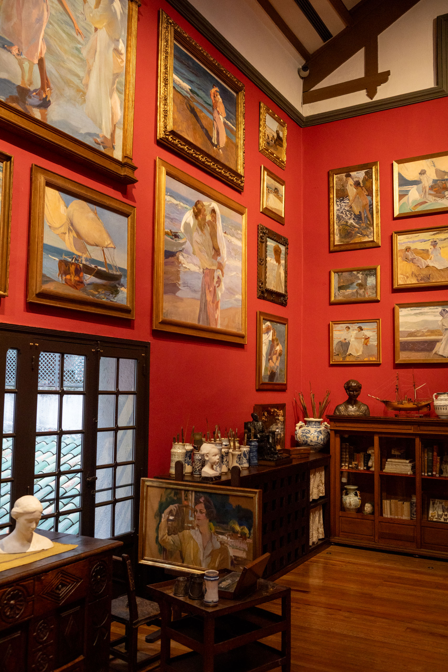 Studio van Sorolla in museum Sorolla met rode muur vol schilderijen en eronder kastjes met allerlei spullen