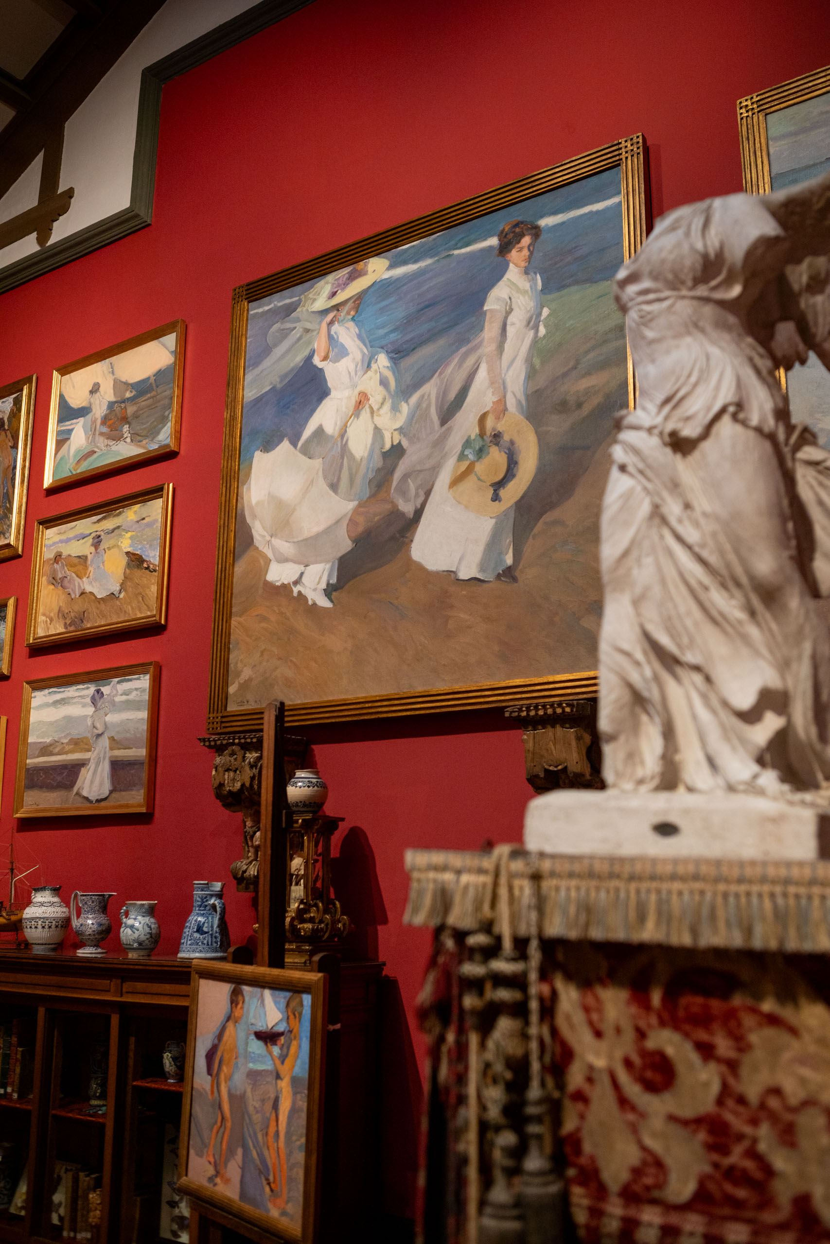 Studio van Sorolla in museum Sorolla met rode muur vol schilderijen en een standbeeld op de voorgrond