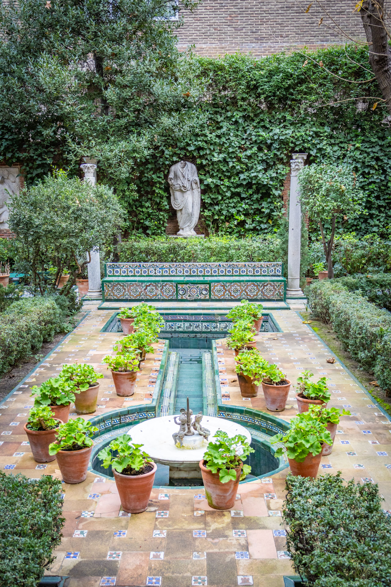 De tuin van Museo Sorolla, met veel groen, standbeeld en vijvertje met fonteintje en Spaanse tegeltjes