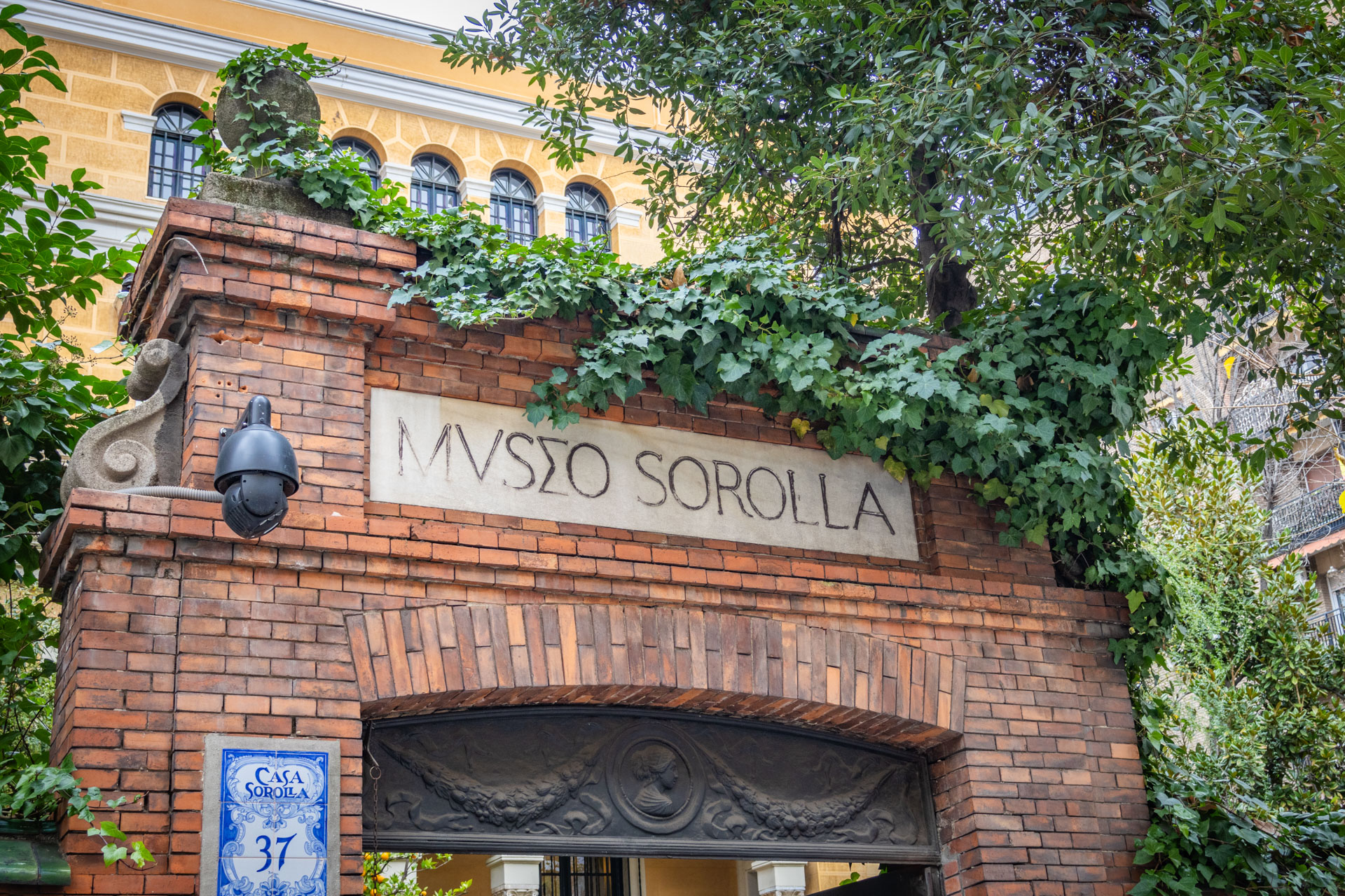 Bakstenen toegangspoort waar in Romeins lettertype 'Museo Sorolla' in staat met erachter een groot geel landhuis.