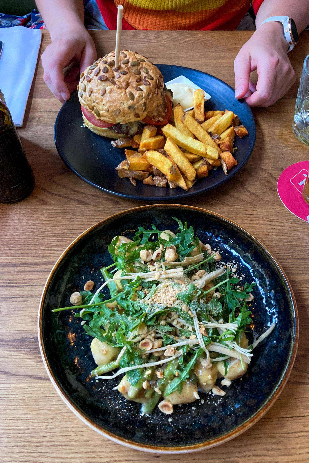 Twee borden op tafel bij BurgerZaken in Leiden met op het voorste bord groente en op het achterste bord een hamburger en frietjes.